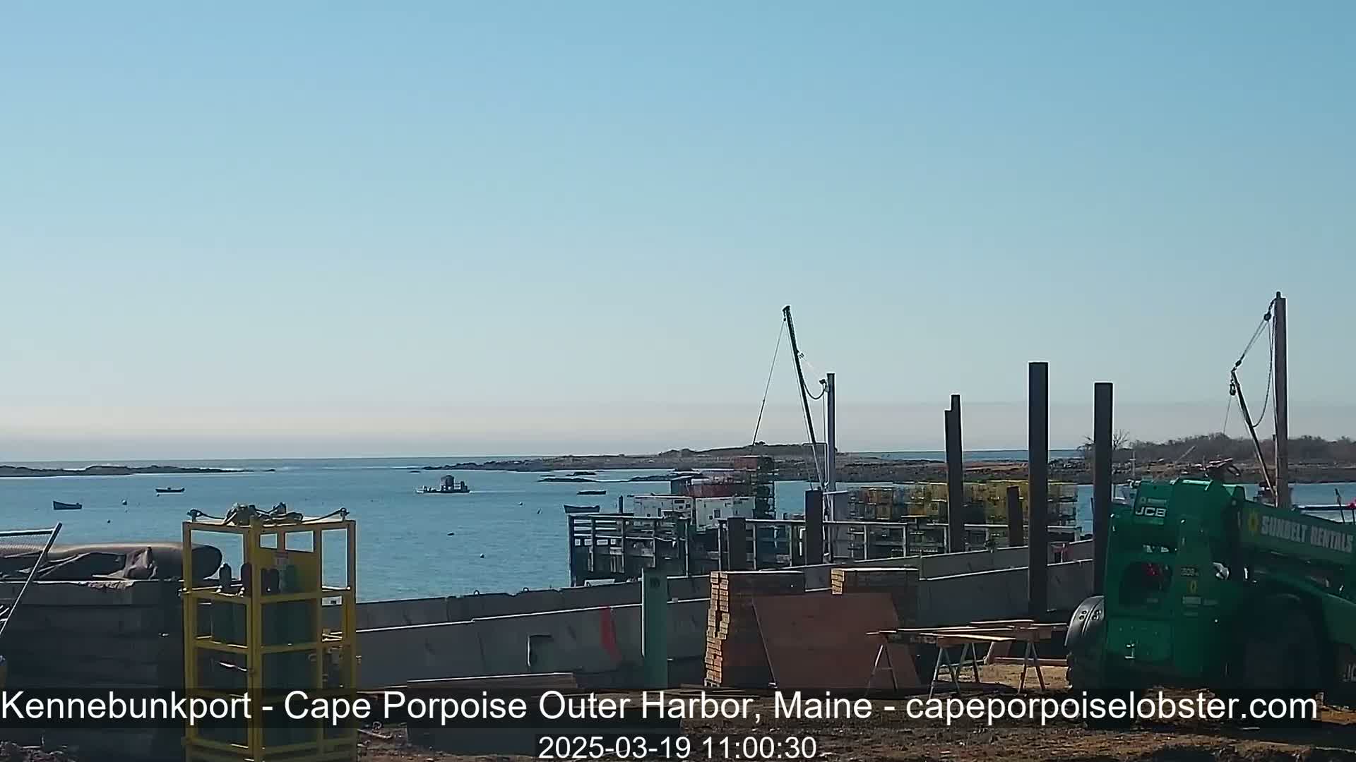 A harbor construction site with calm blue water, a few boats, and clear skies.