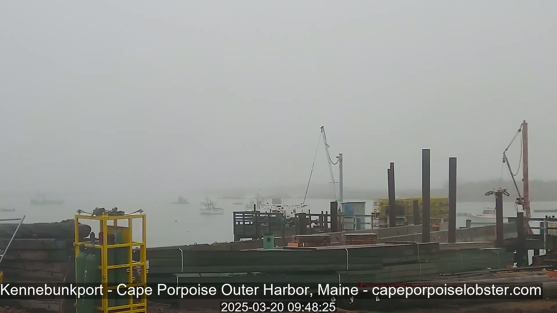 A foggy harbor scene shows several boats moored at a dock under construction, with additional boats visible in the hazy distance.