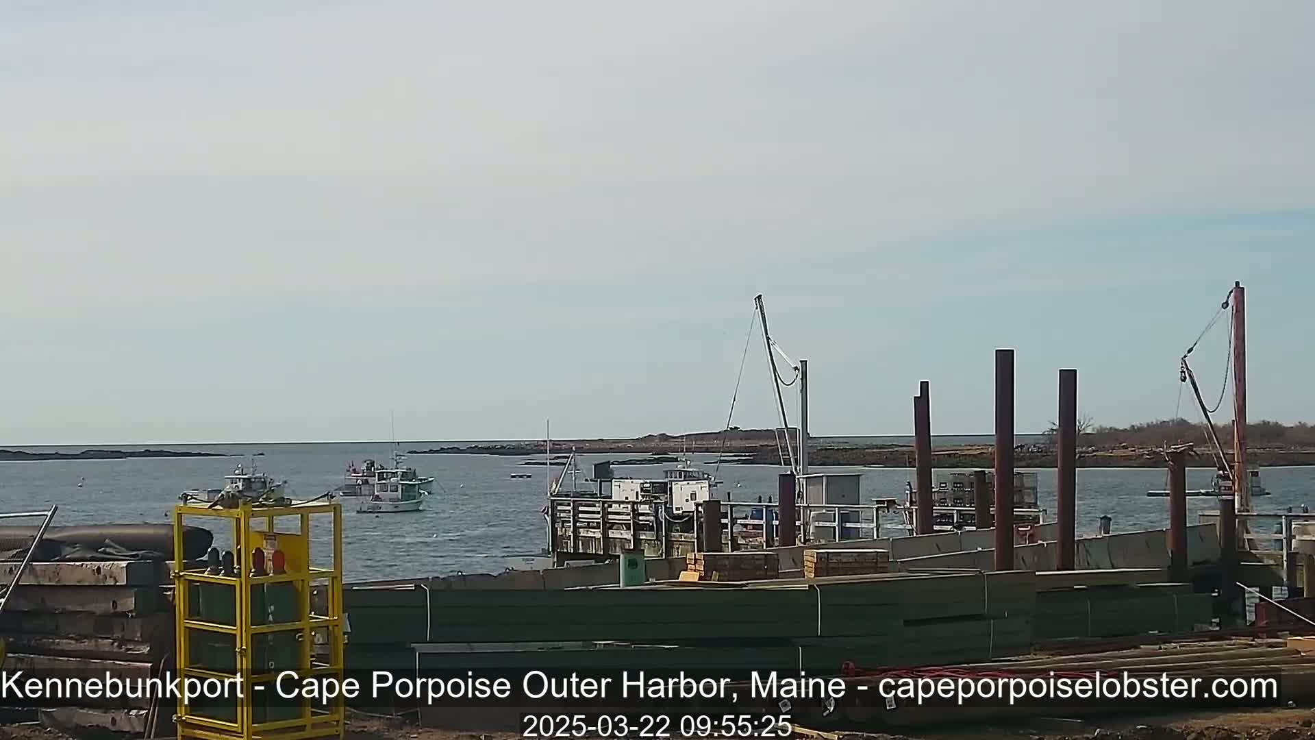 Several boats are in a harbor under a mostly clear sky, with construction underway on a dock in the foreground.