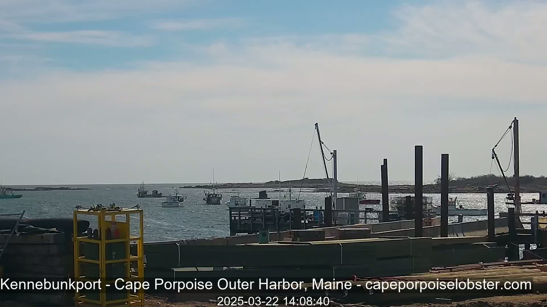 Several fishing boats are moored in a harbor under a partly cloudy sky, with construction underway on a nearby dock.