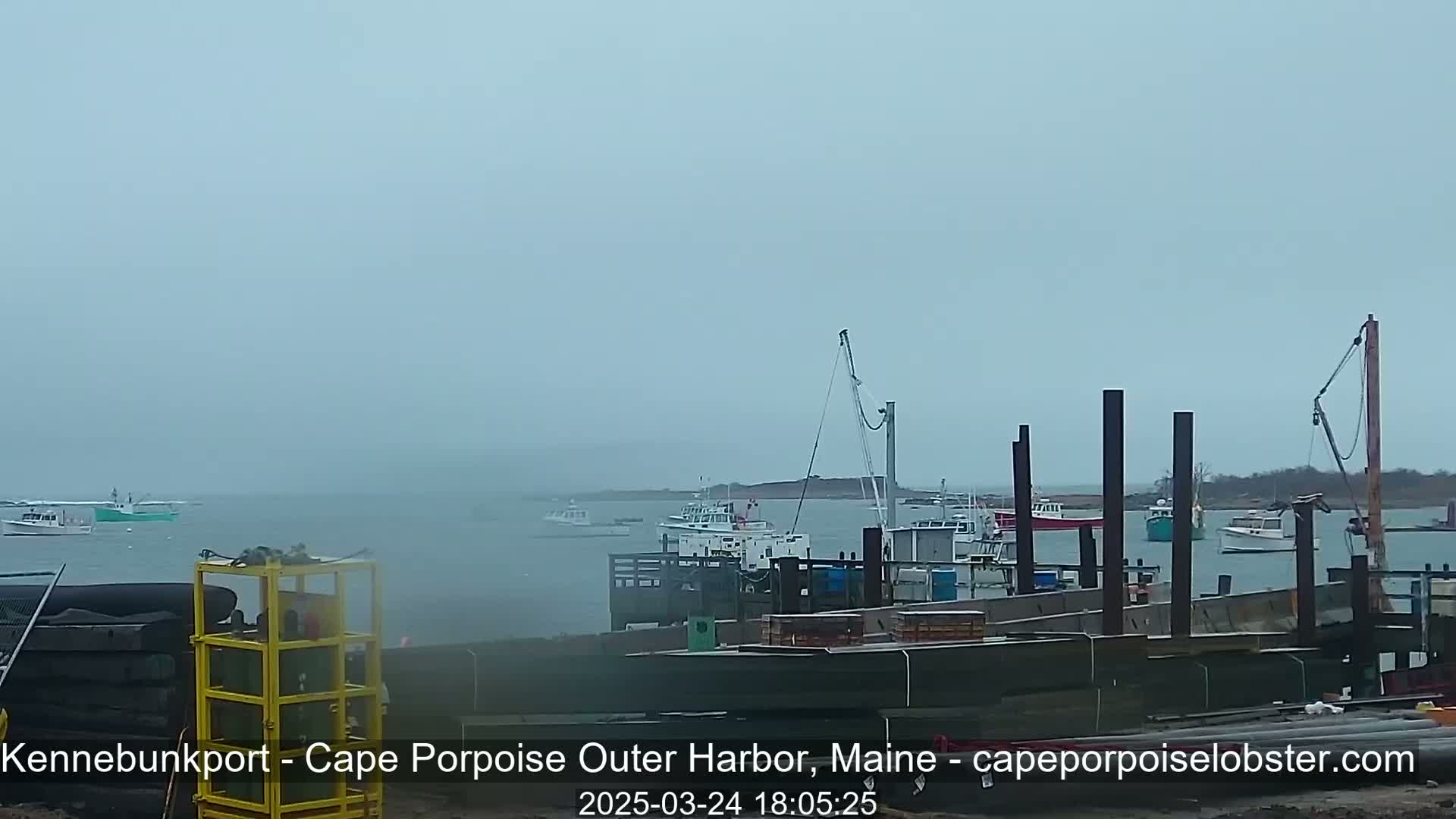 Several boats are moored at a harbor under foggy conditions.