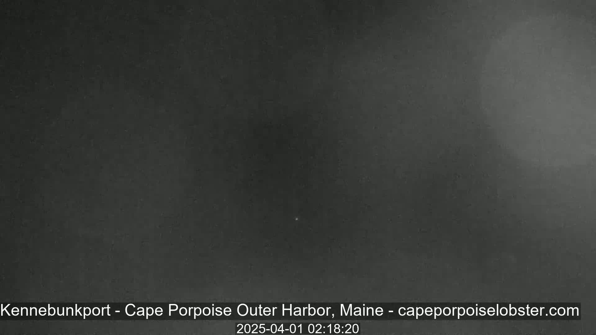A dark, nighttime image shows a single, faint light in the center of a mostly uniform gray-black sky.