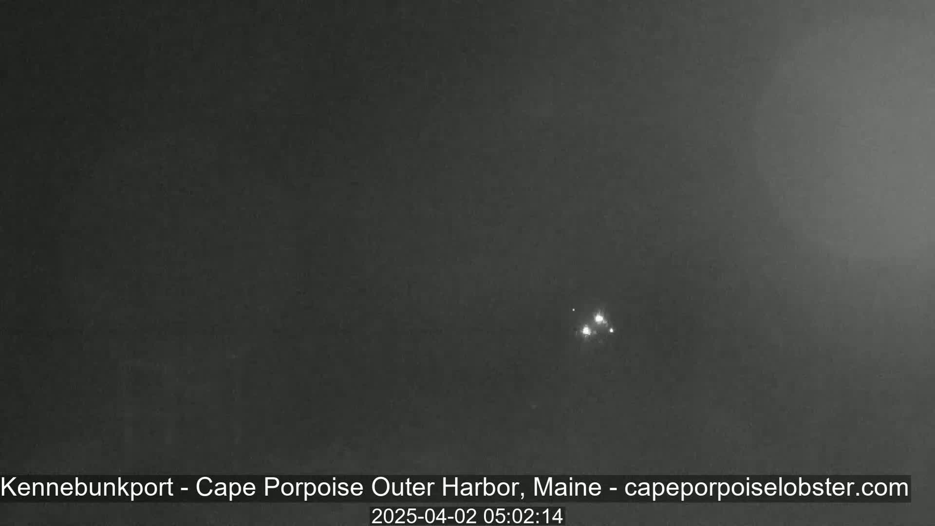 A dark, nighttime image shows a few faint lights in the distance under a cloudy sky.