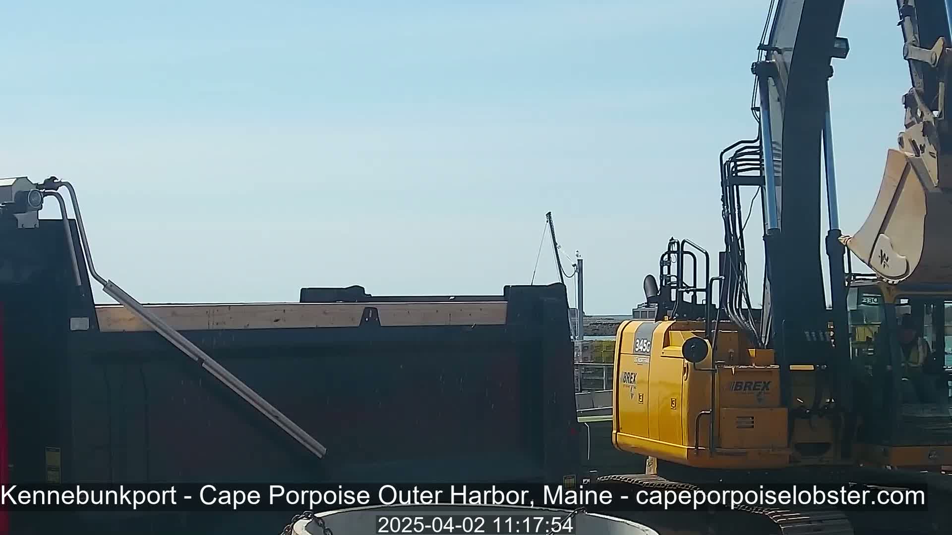A yellow excavator is parked next to a dark-colored dump truck under a clear, bright blue sky.