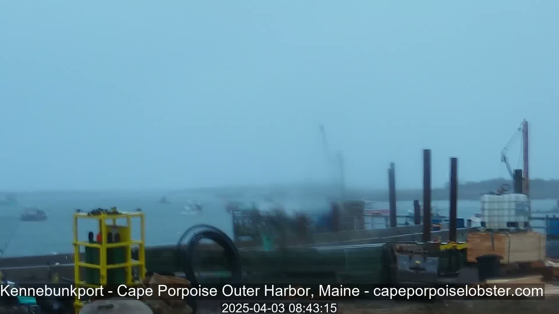 A hazy, overcast day shows a harbor with several boats and construction equipment near a dock.