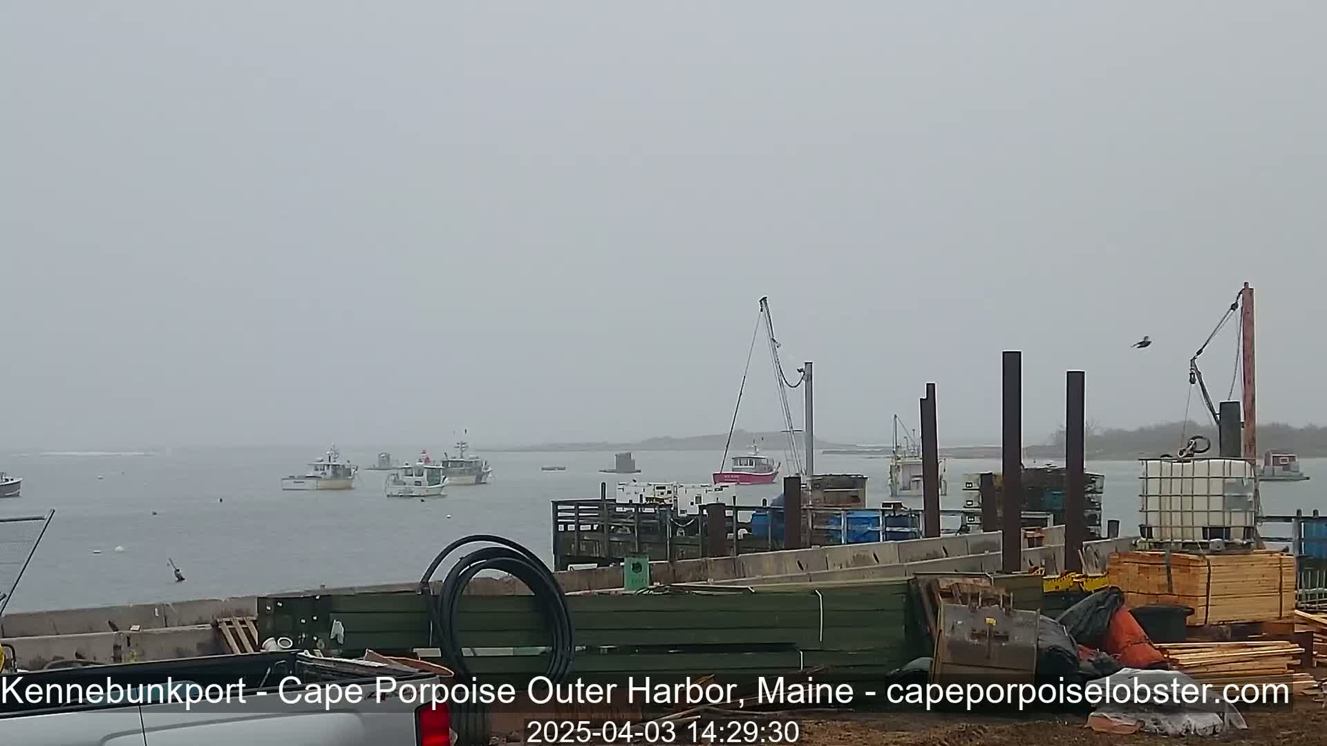 Several boats are in a harbor under an overcast sky, with construction or repair work underway on a pier in the foreground.