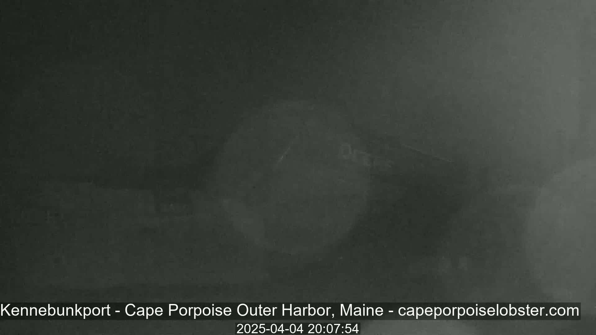 A dark, foggy scene shows a dimly lit harbor at night.