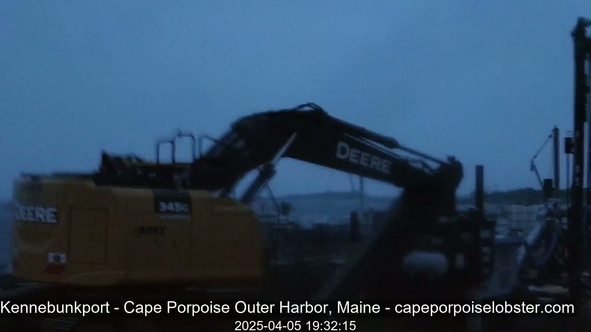 A yellow and black excavator is visible in a harbor under a twilight sky.