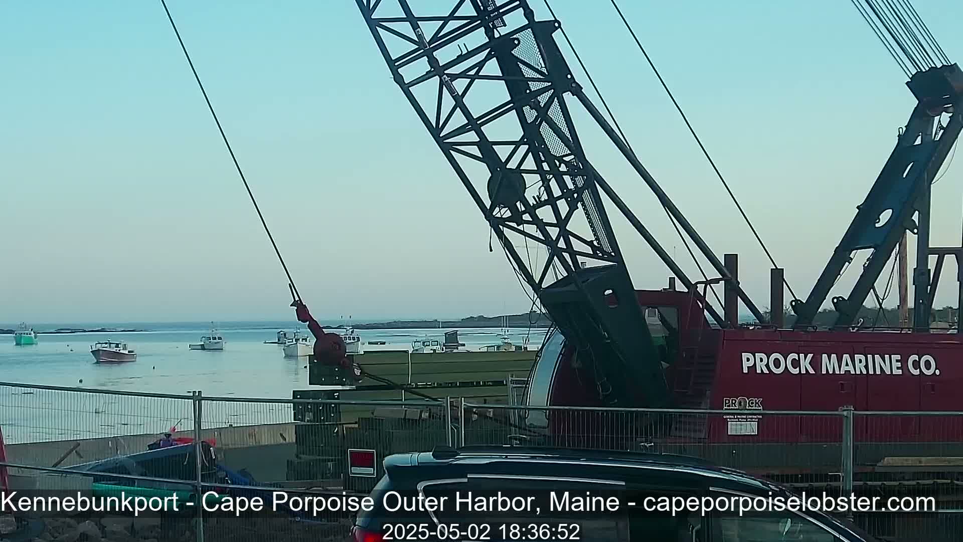 A large red crane is positioned near a harbor filled with several small boats under a clear, light-blue sky.