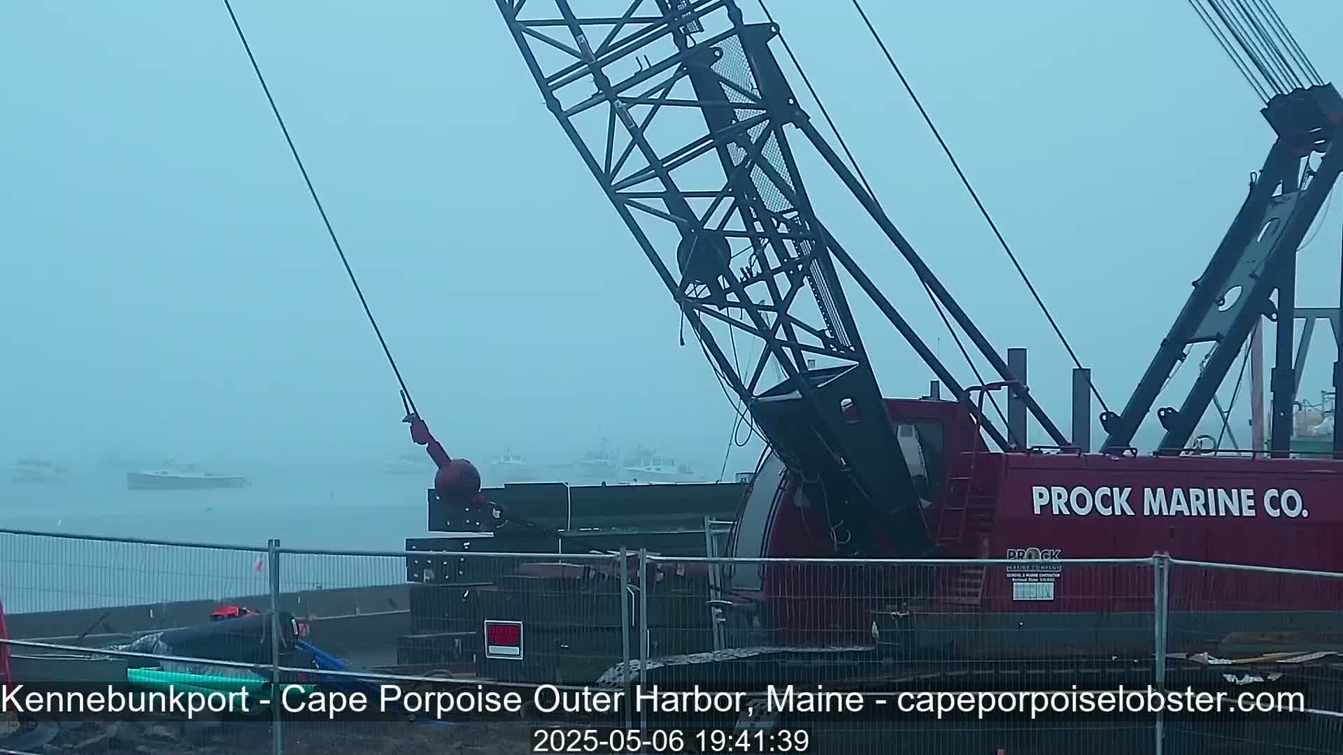 A large red crane is positioned near a harbor in foggy conditions, with several boats visible in the distance.