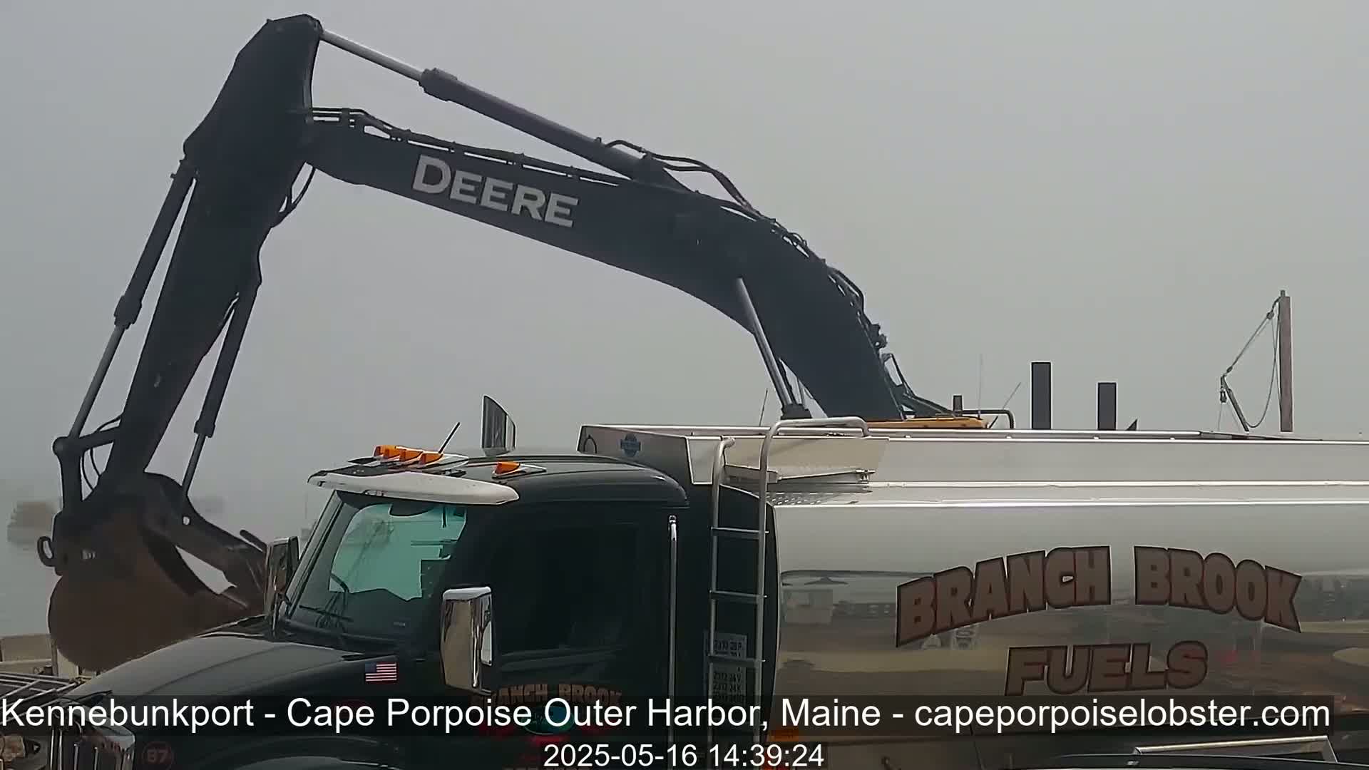 A large Deere excavator is at a construction site on a foggy day.