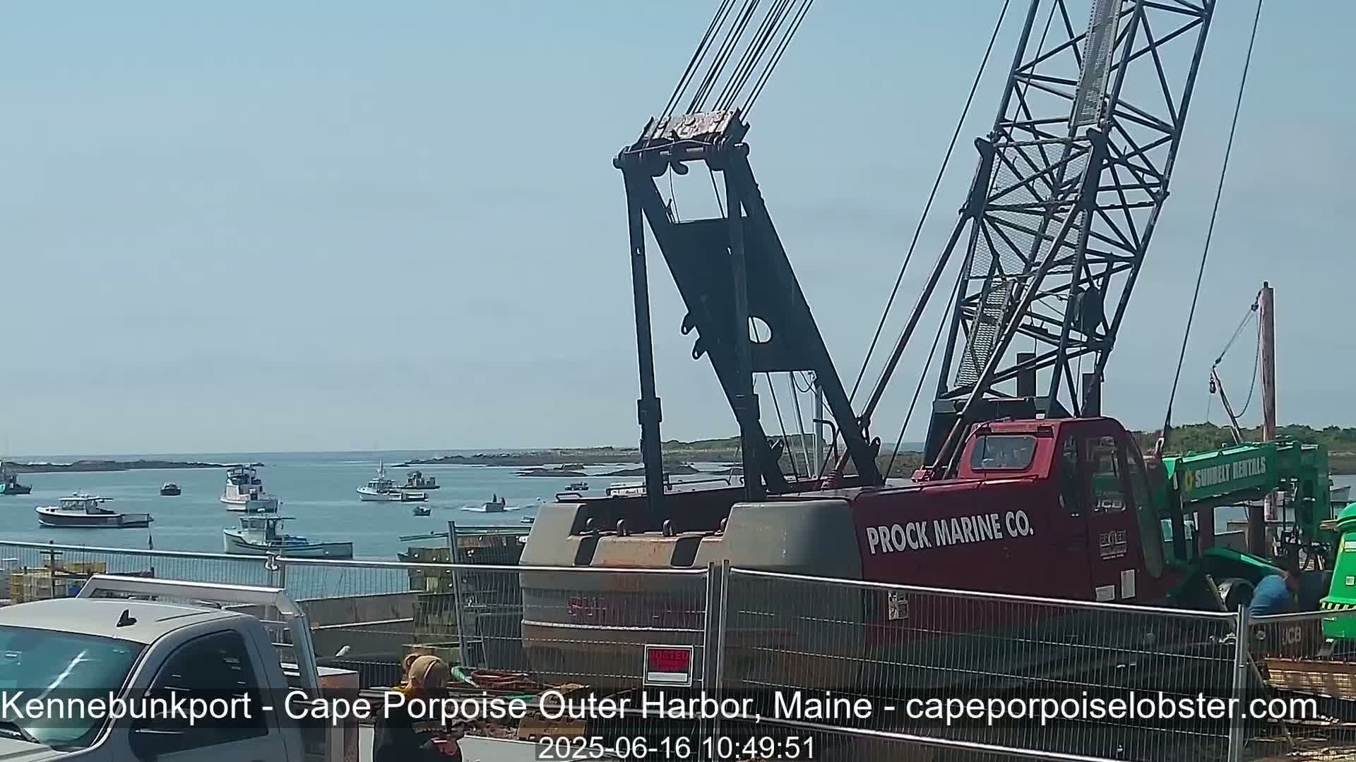 A large red crane is situated near a harbor filled with numerous small boats on a sunny day.