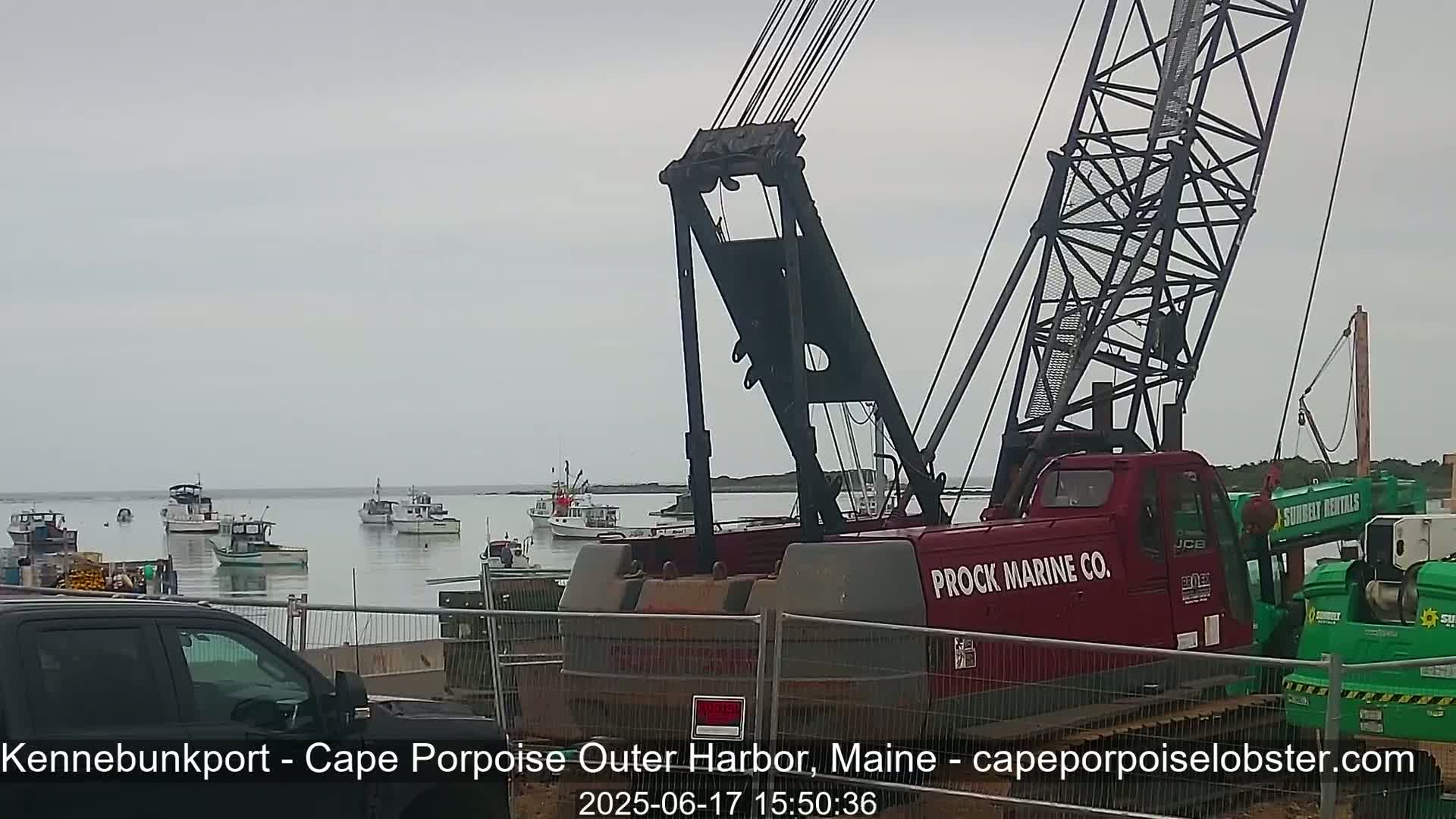 A large red crane is positioned near a harbor with numerous small boats under an overcast sky.