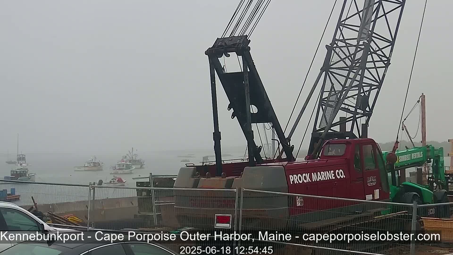 A large red crane is positioned near a harbor in foggy conditions, with several boats visible in the distance.