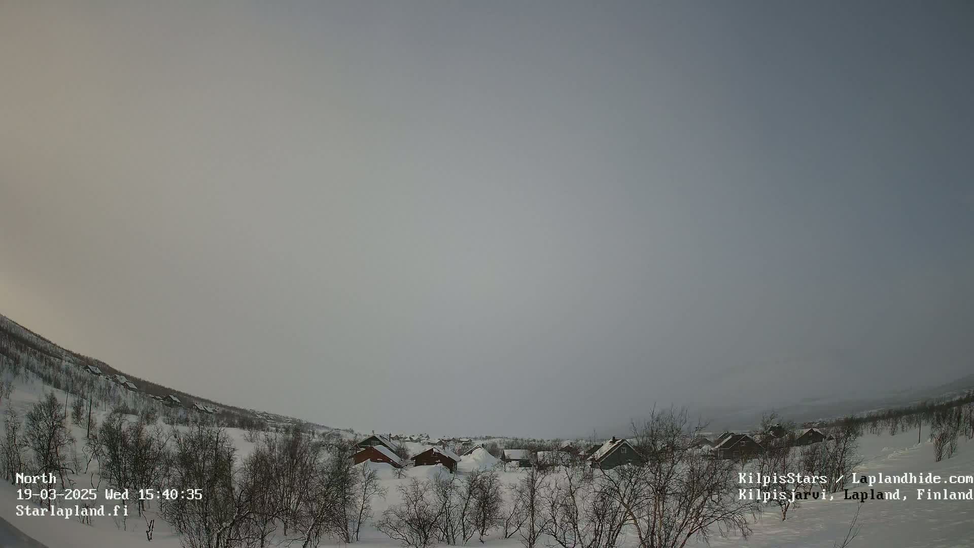 A snow-covered village nestled in a hilly landscape under a hazy, overcast sky.