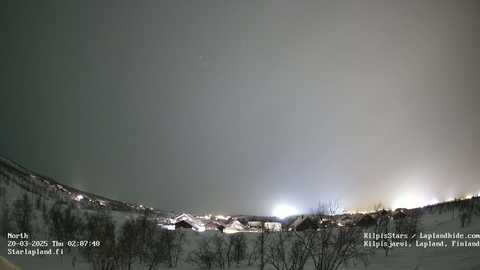 A snow-covered village is illuminated at night under a hazy, overcast sky.