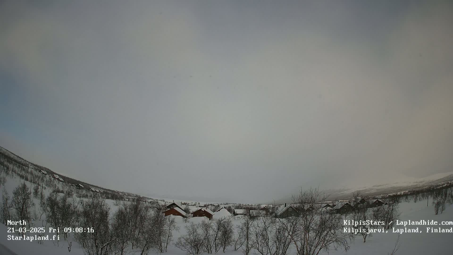 A snowy landscape with a small cluster of houses under a hazy, overcast sky.