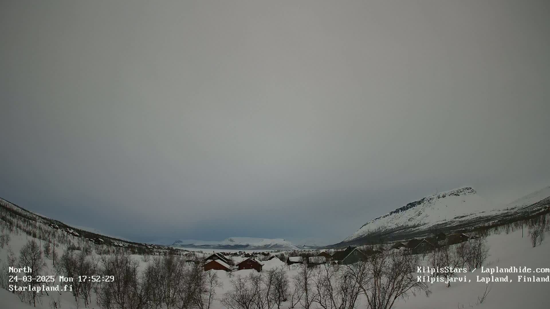 A snow-covered village nestled between snow-dusted mountains under a cloudy sky.