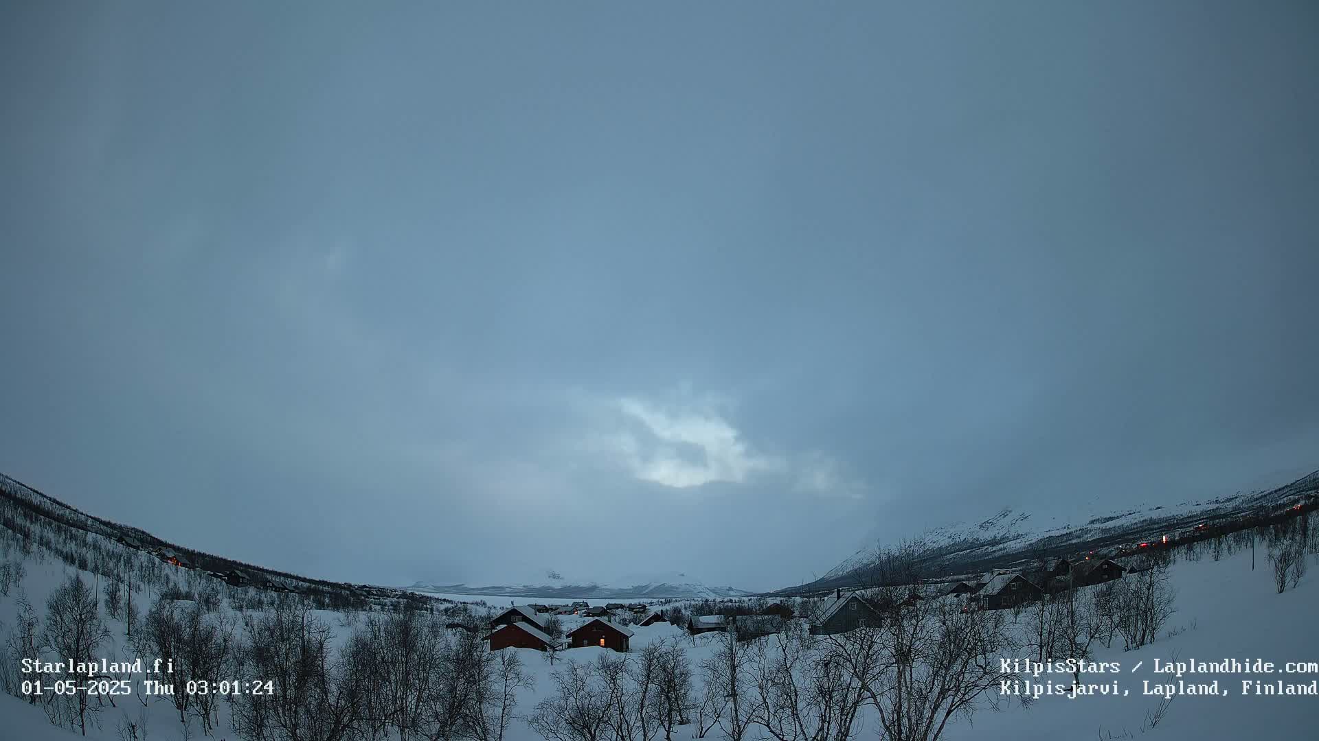 A snow-covered village nestled in a valley between mountains under a pale, overcast sky.