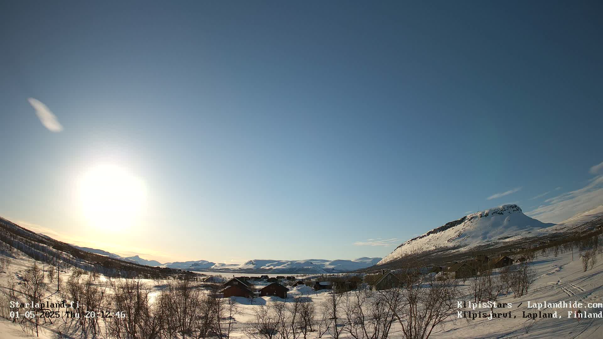 A small snow-covered village sits in a valley between snow-capped mountains under a bright, clear sky.