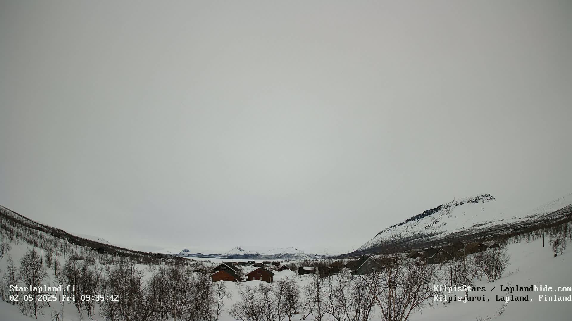 A small snow-covered village nestled in a valley between snow-capped mountains under an overcast sky.