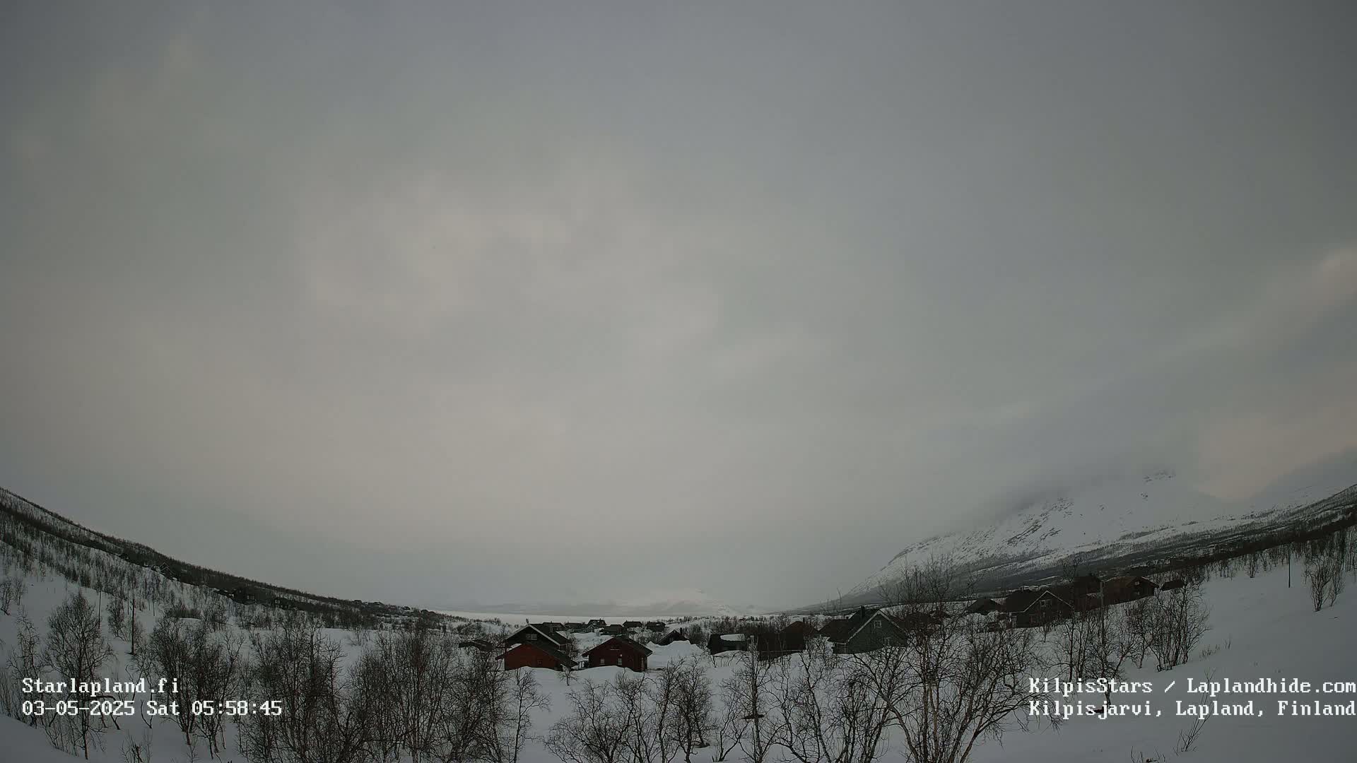 A snow-covered landscape with a few small buildings is visible under an overcast sky.