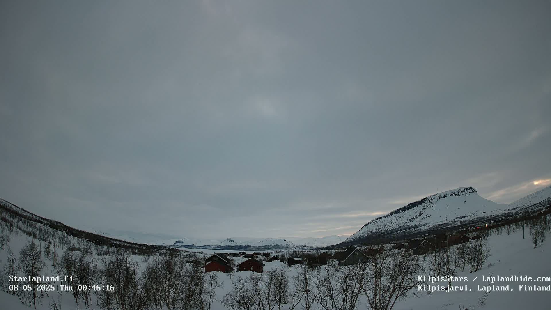 A snow-covered village nestled in a valley between snow-capped mountains under a cloudy, overcast sky.