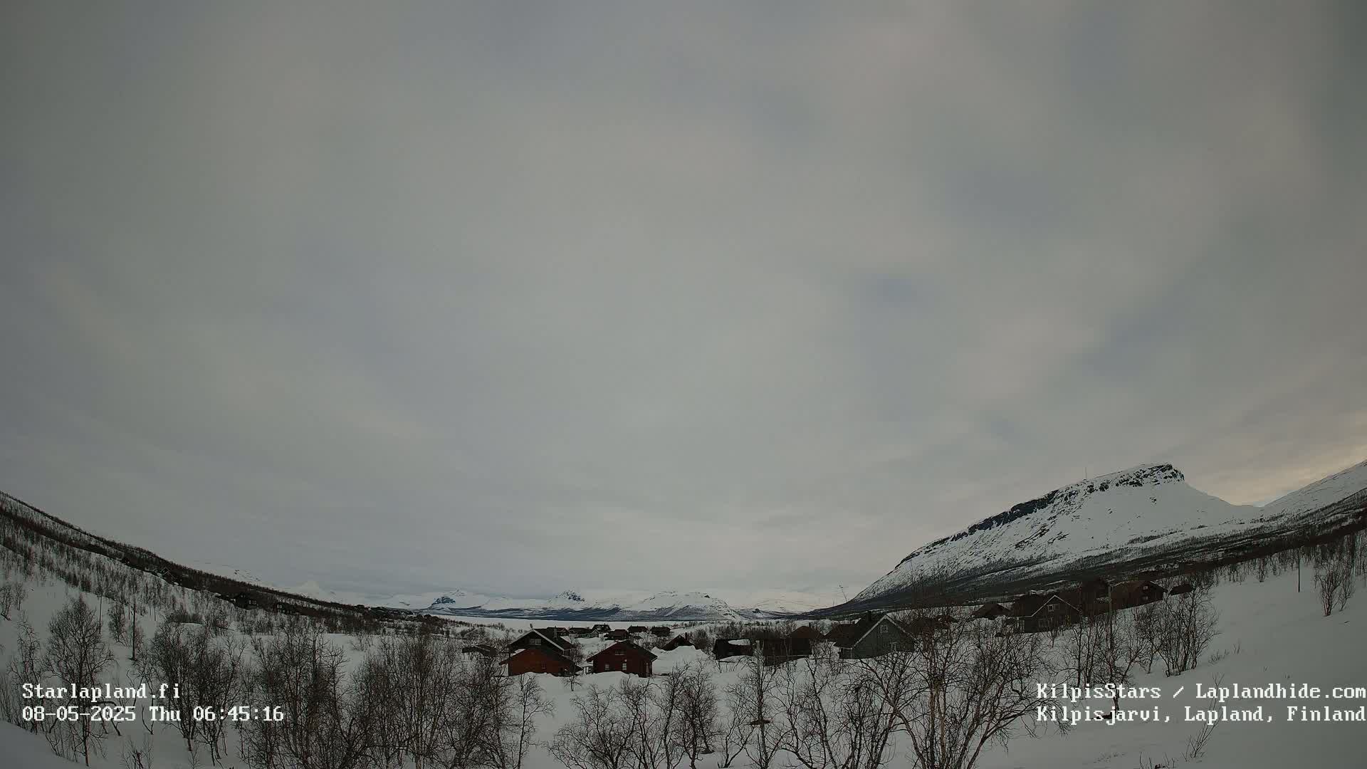 A snow-covered village nestled in a valley between mountains under a cloudy sky.