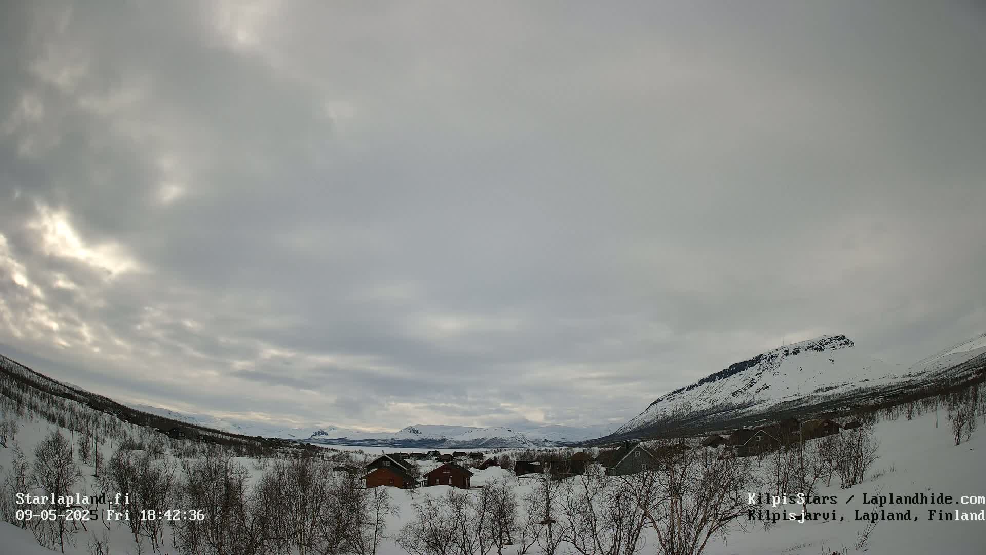 A snow-covered village nestled in a valley between snow-dusted mountains under a cloudy sky.