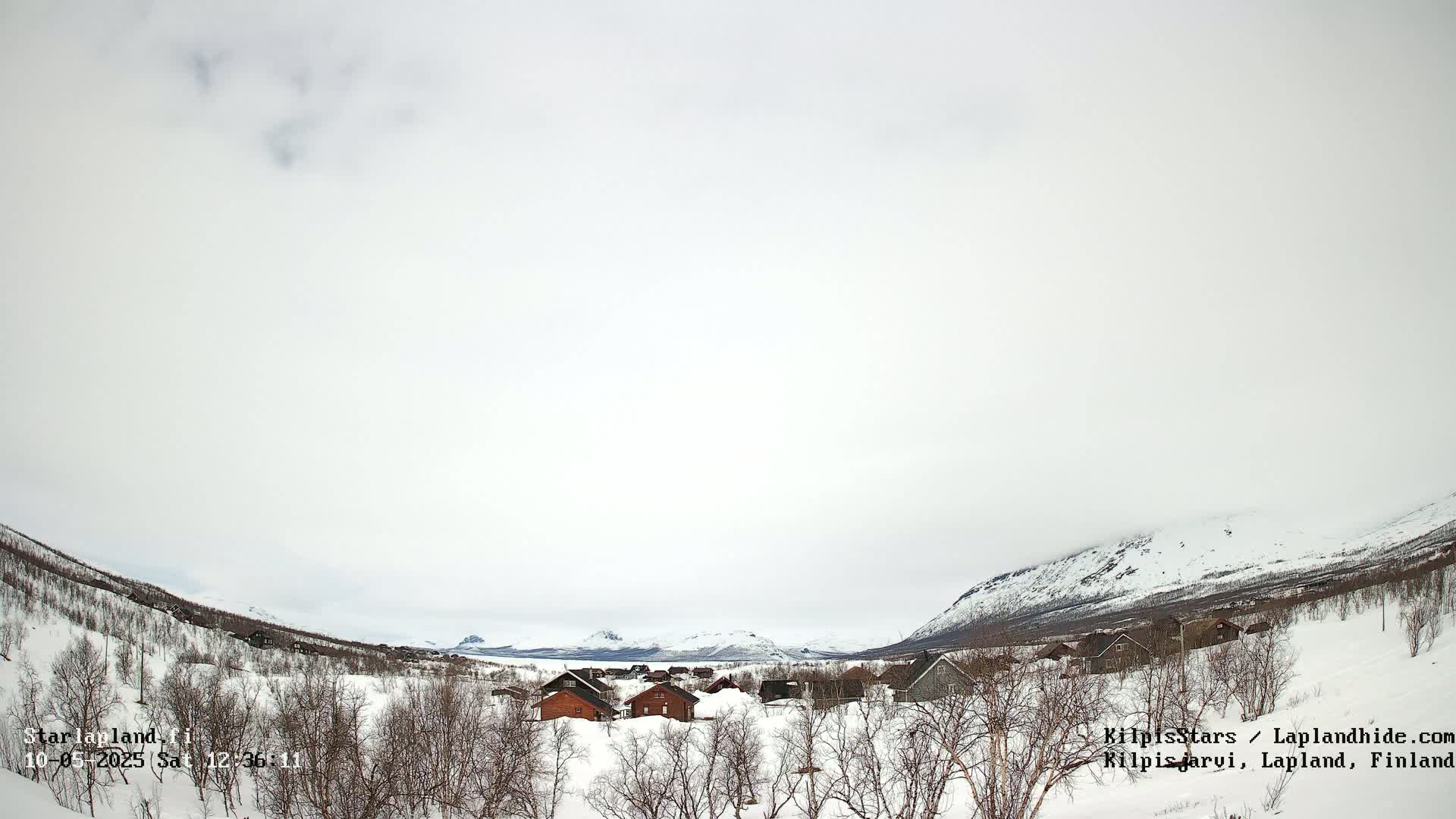 A small snow-covered village nestled in a valley between snow-capped mountains under an overcast sky.