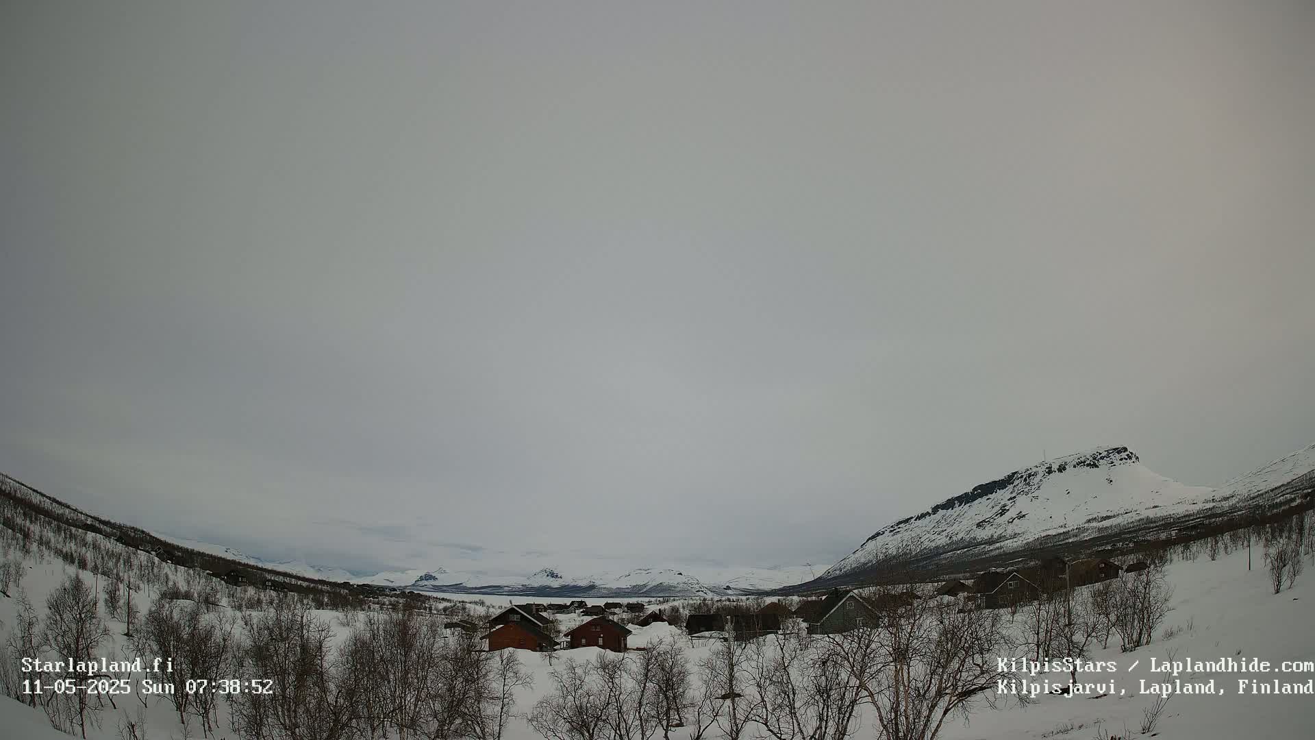 A snow-covered village nestled in a valley between snow-capped mountains under an overcast sky.