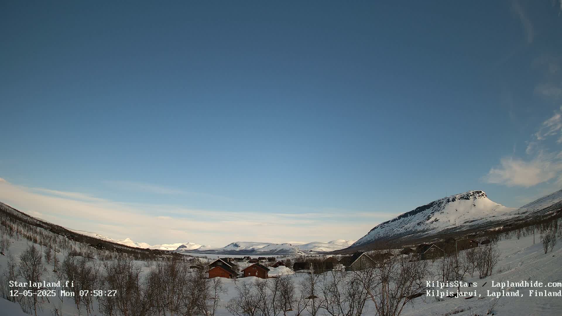 A snow-covered village nestled in a valley between snow-capped mountains under a clear blue sky.