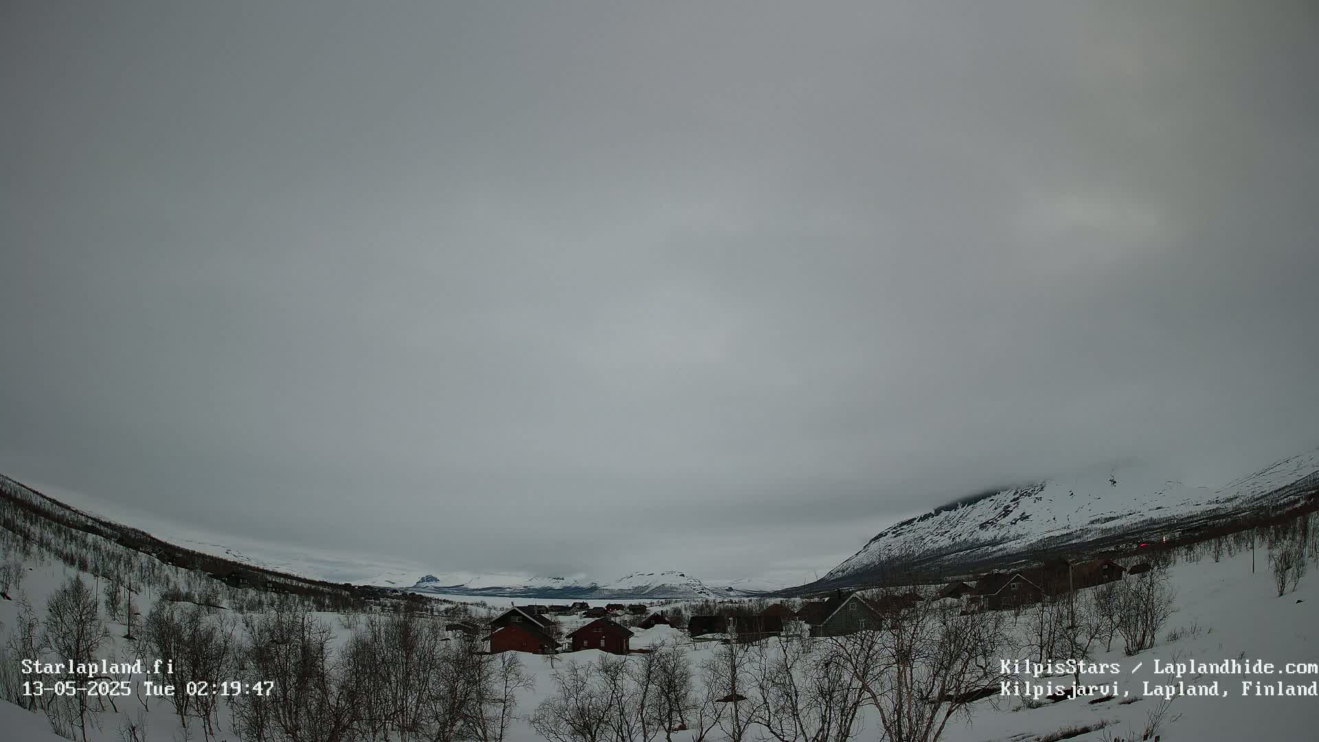 A snow-covered landscape with small houses and distant mountains under an overcast sky.