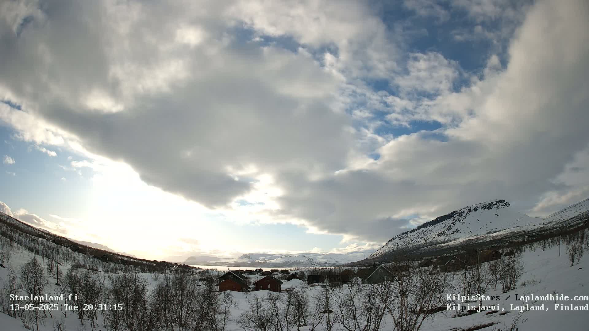 A snowy, sparsely populated village nestled in a valley between snow-covered mountains under a partly cloudy sky.