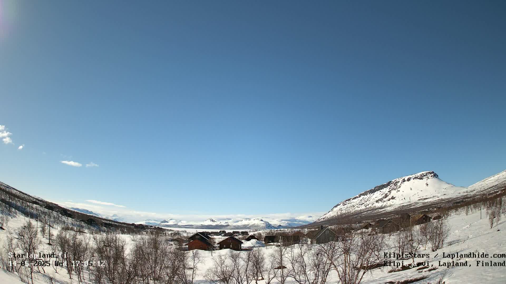 A snow-covered village nestled in a valley between snow-capped mountains under a clear blue sky.