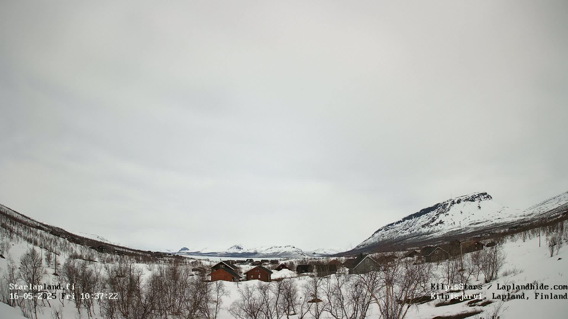 A snow-covered village nestled in a valley between snow-capped mountains under an overcast sky.
