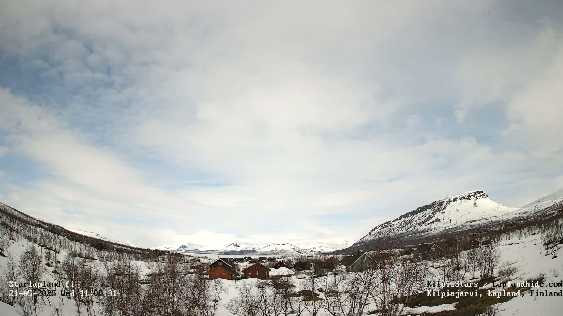 A small village nestled in a snow-covered valley between mountains under a partly cloudy sky.