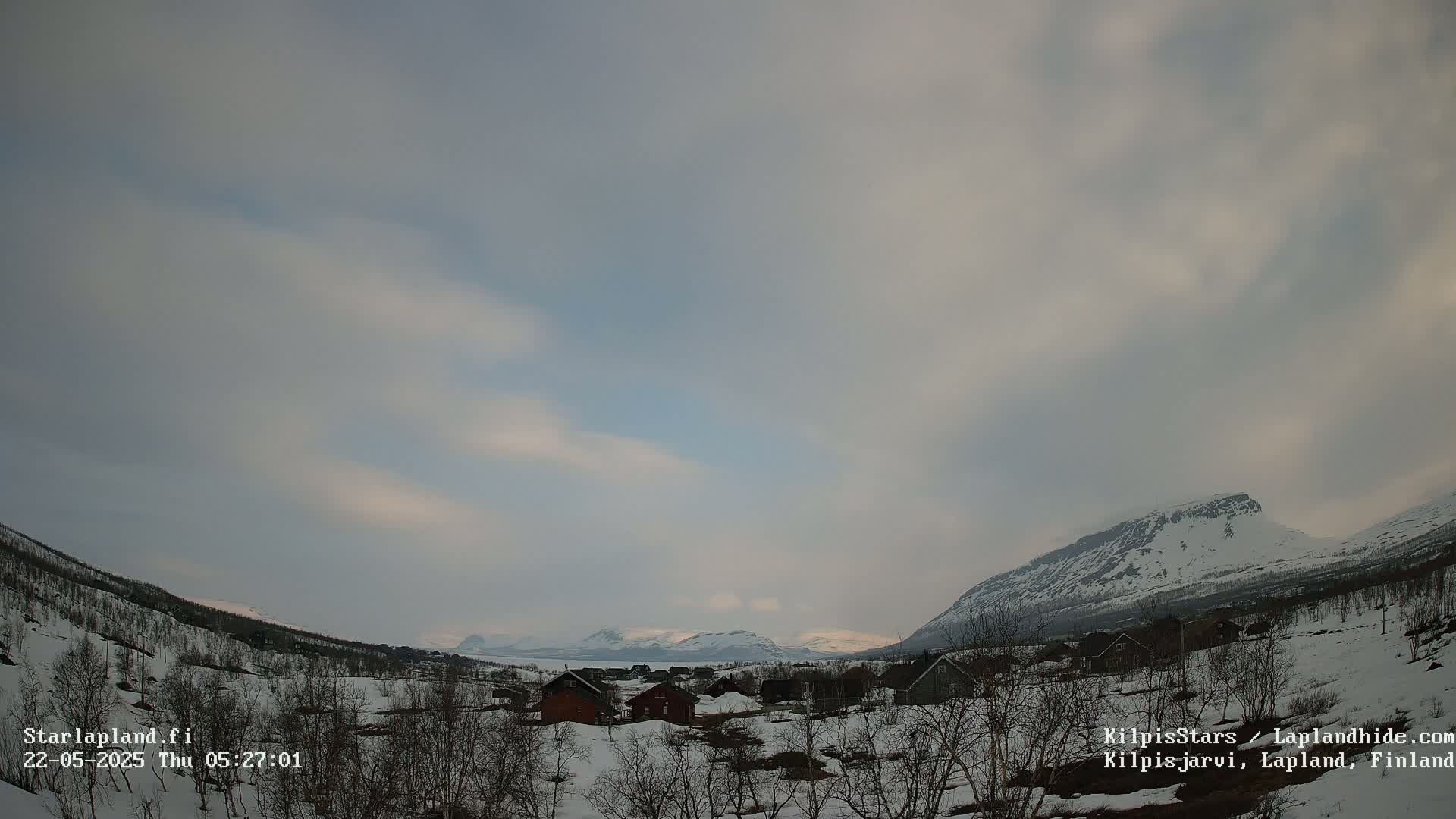 A snow-covered village nestled in a valley between mountains under a mostly cloudy sky.