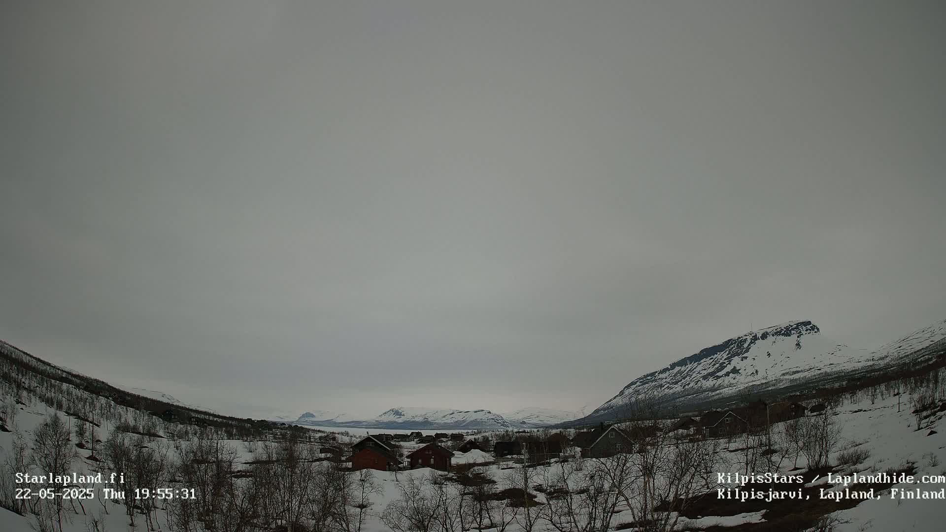 A snow-covered village nestled in a valley between snow-capped mountains under an overcast sky.