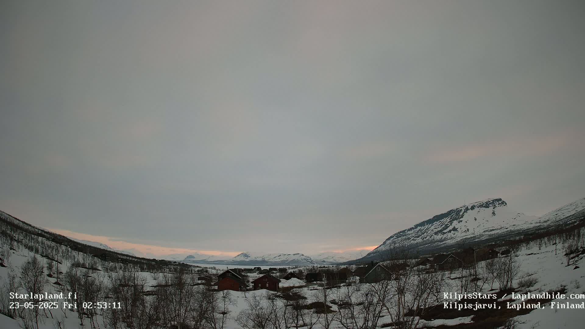 A snow-covered village nestled in a valley between mountains under a pale, overcast sky.