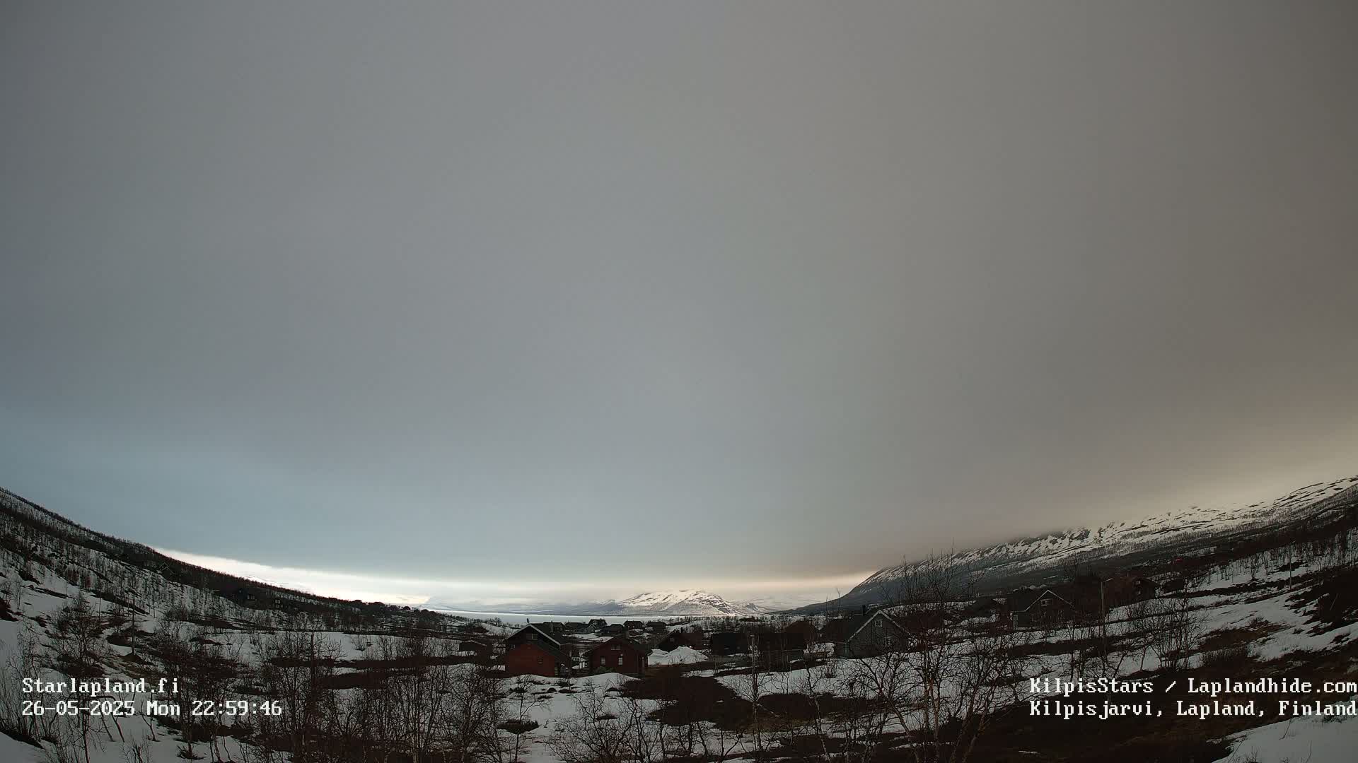 A snow-covered village nestled in a valley, under a mostly cloudy, gray sky, with mountains in the background.