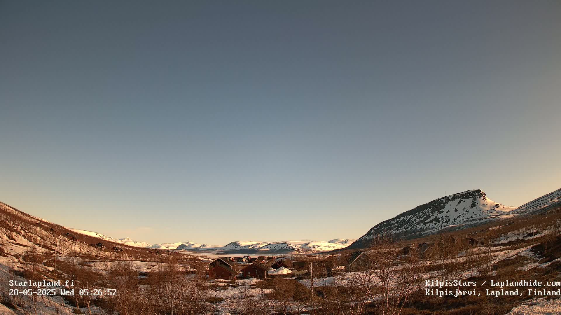 A small village nestled in a valley between snow-capped mountains under a clear, twilight sky.