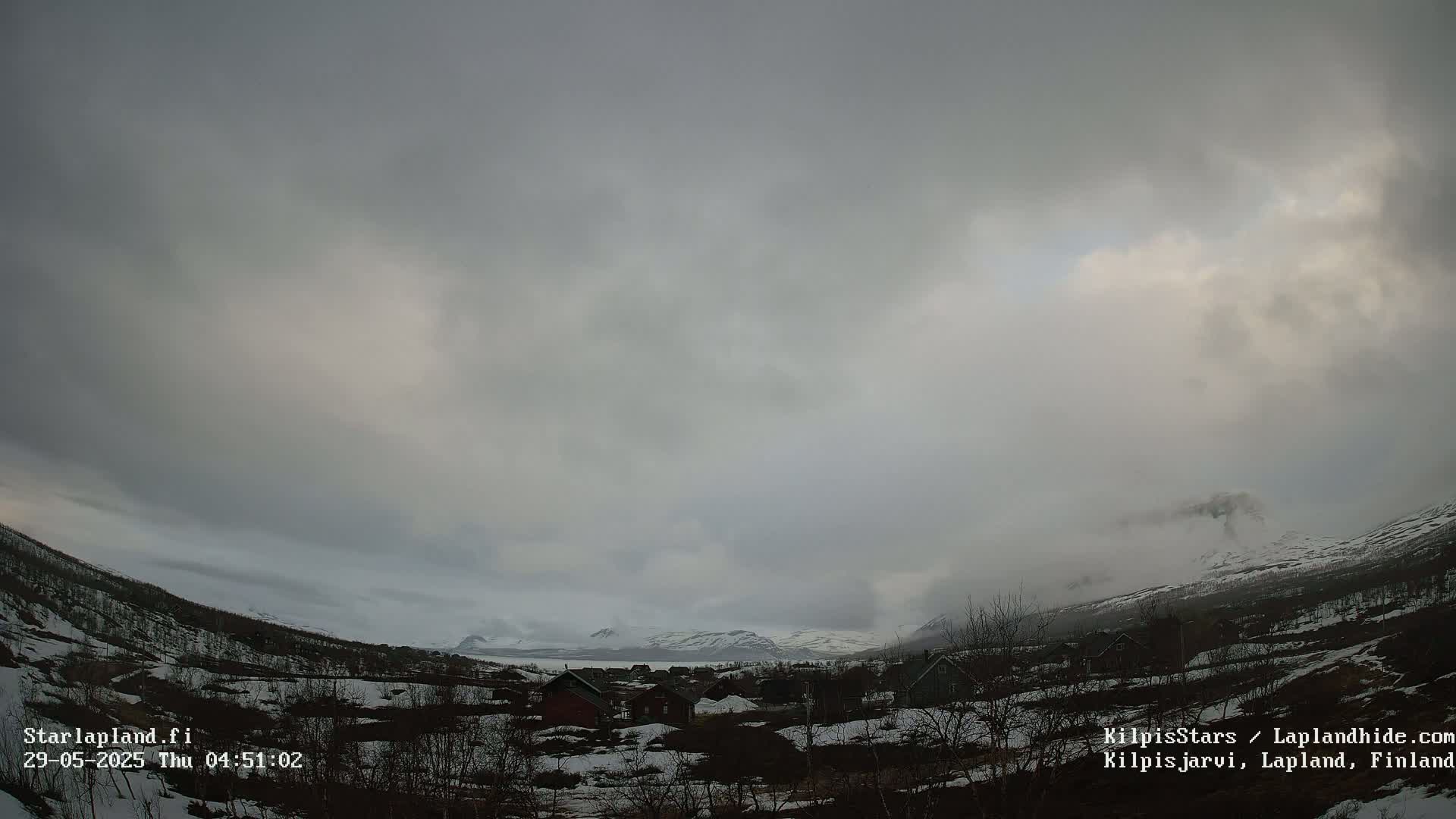 A small village nestled in a valley between snow-covered mountains under a cloudy, overcast sky.