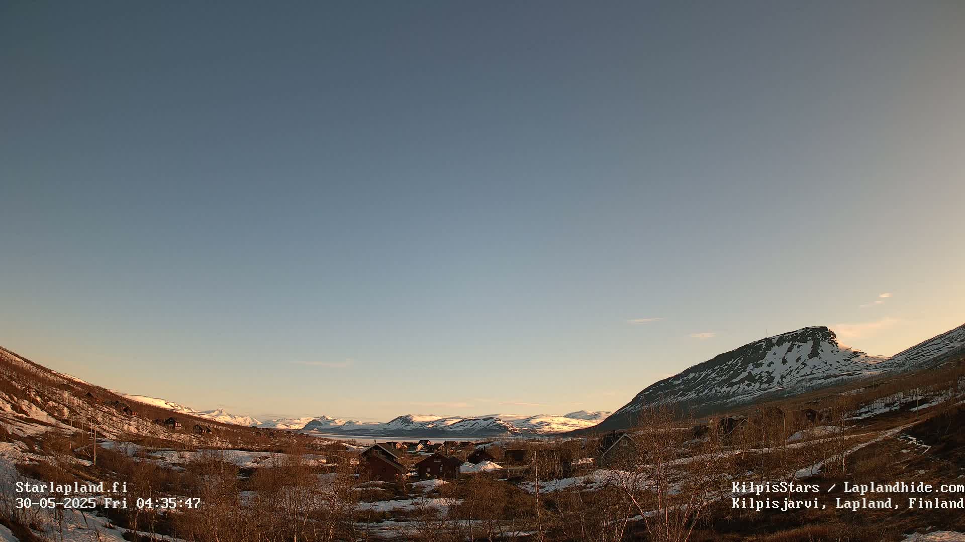 A small village nestled in a valley between snow-capped mountains under a clear, twilight sky.