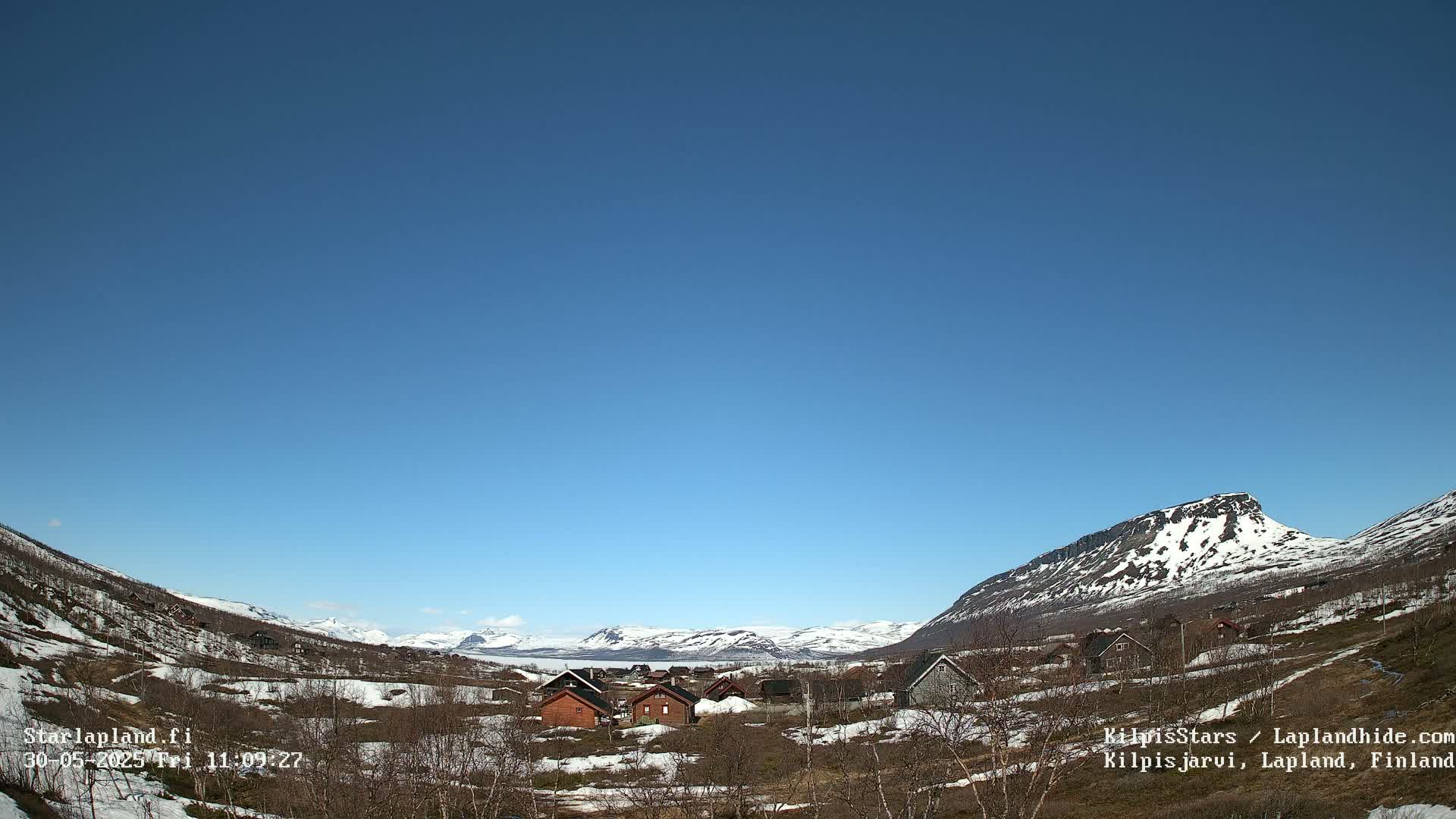 A small village nestled in a valley between snow-capped mountains under a clear blue sky.