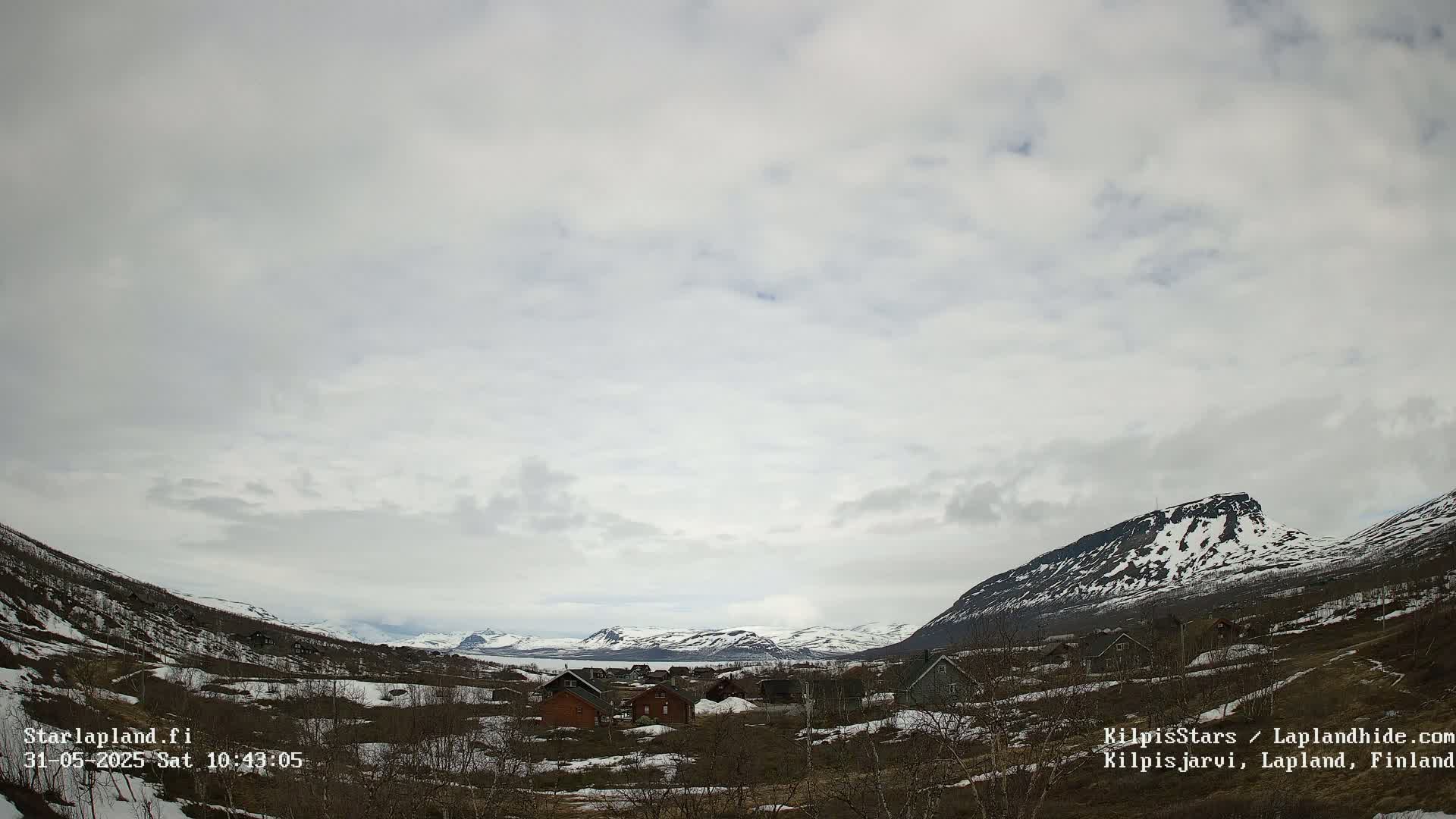 A small village nestled in a valley between snow-capped mountains under a mostly cloudy sky.