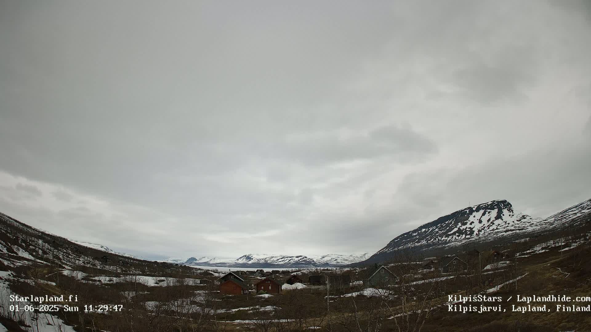 A small village nestled in a valley between snow-capped mountains under an overcast sky.