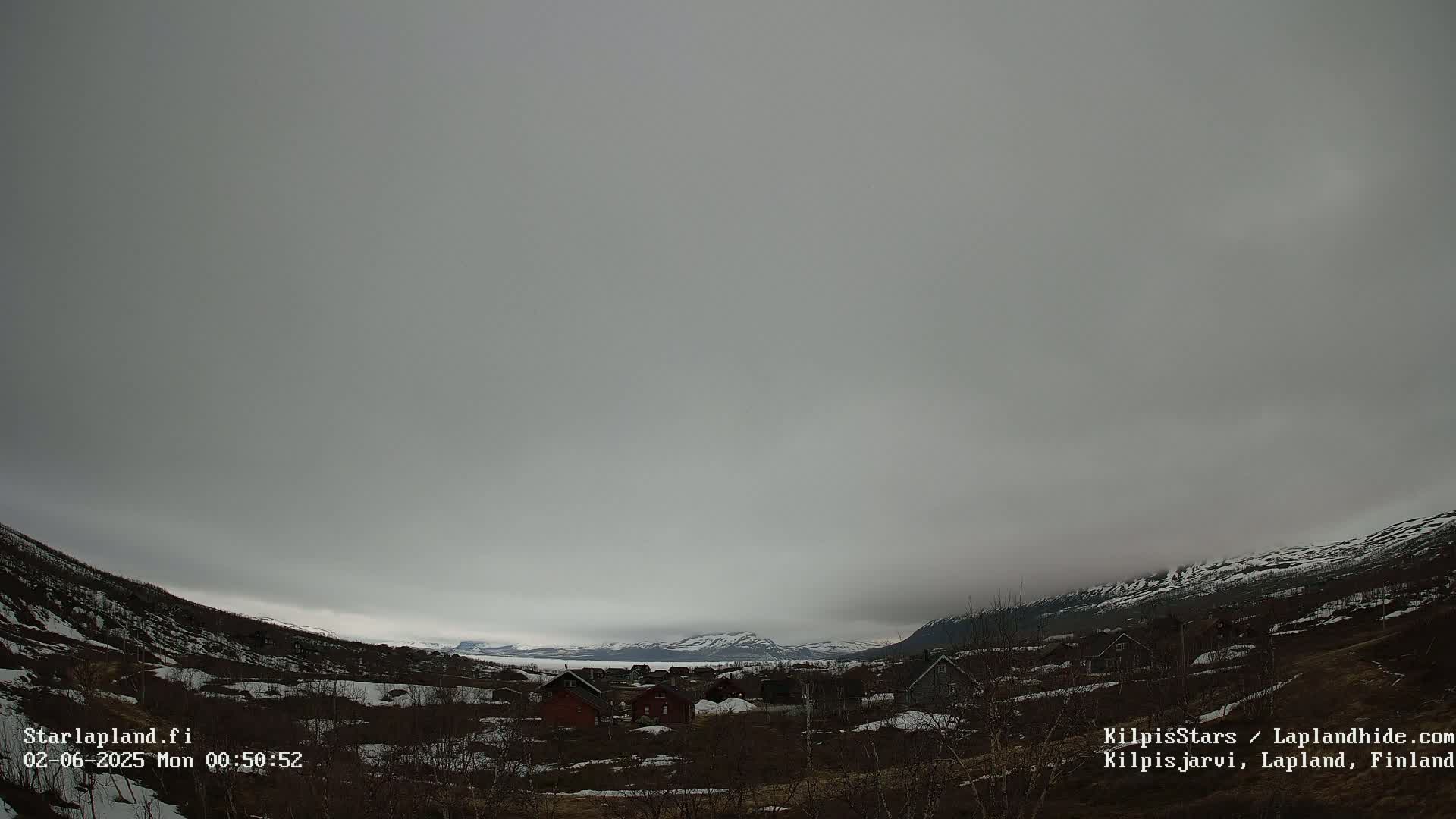 A small village nestled in a valley between snow-dusted mountains under an overcast sky.