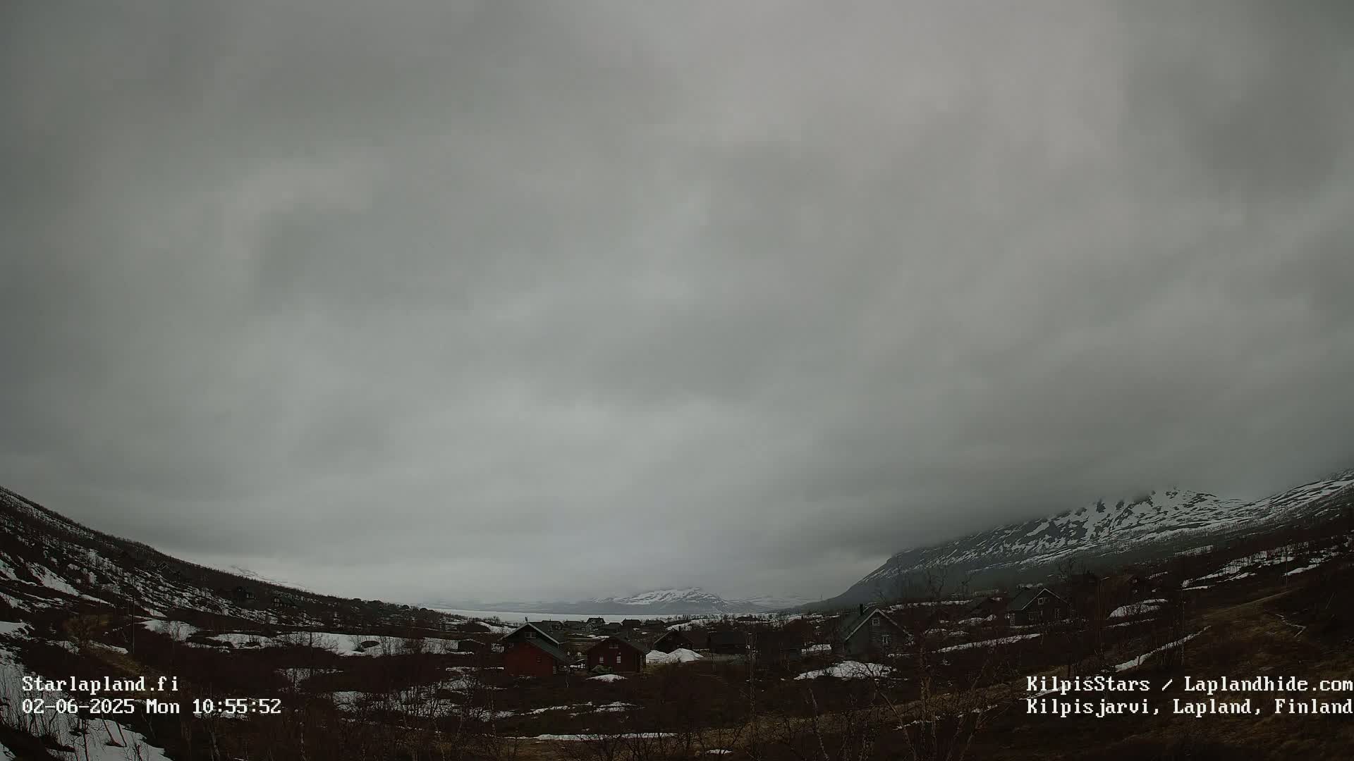 A cloudy, overcast day reveals a small village nestled in a valley between snow-dusted mountains.