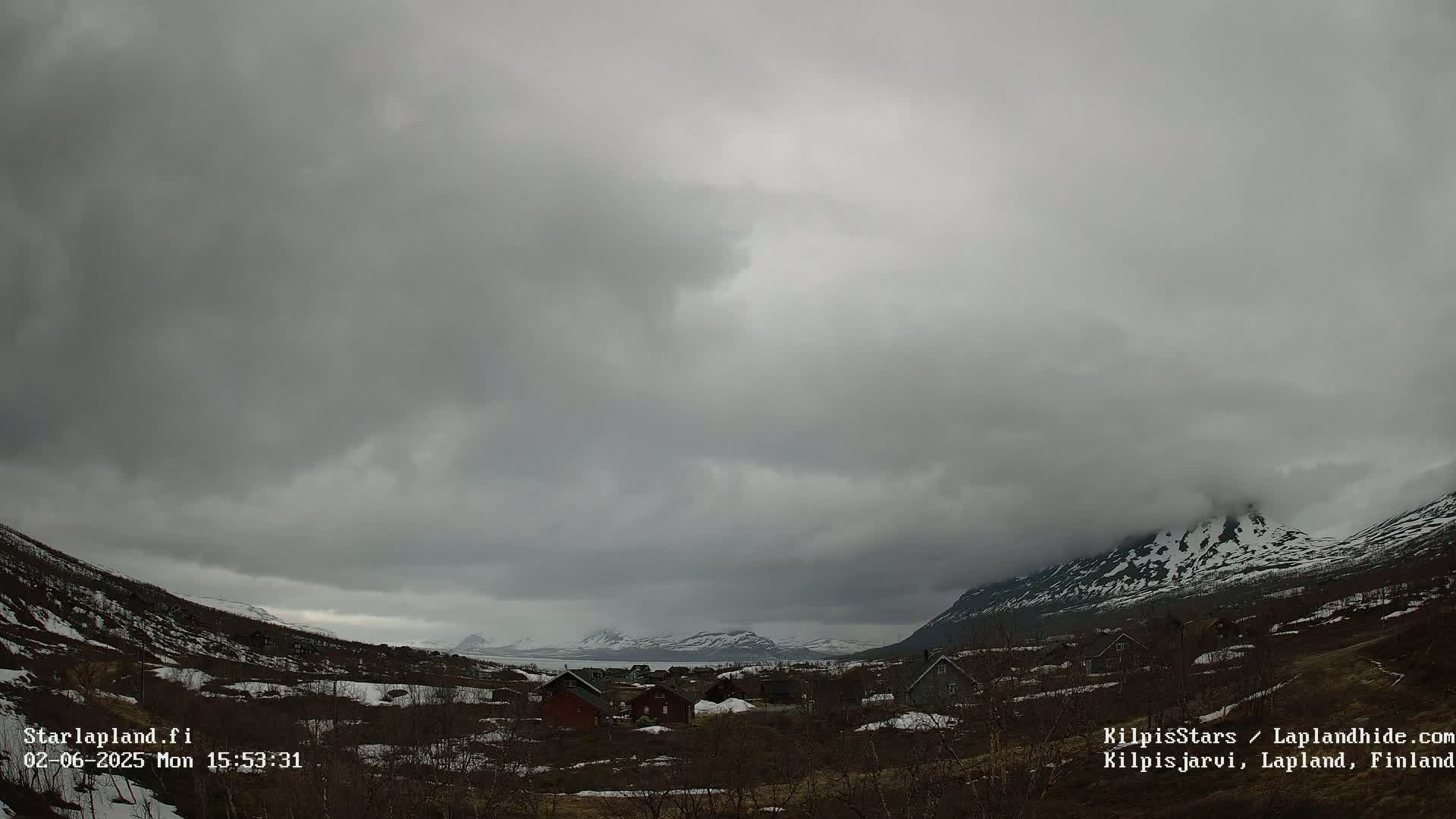 A small village nestled in a valley between snow-capped mountains under an overcast sky.